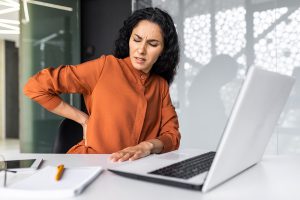 Woman at a desk holding her back in pain, seeking a chiropractor in Knoxville for professional neck pain relief in Knoxville TN.